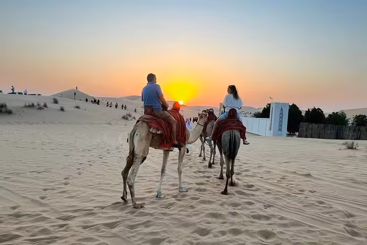 Couple riding camels at sunset across Abu Dhabi white sand dunes on a scenic desert safari camel ride