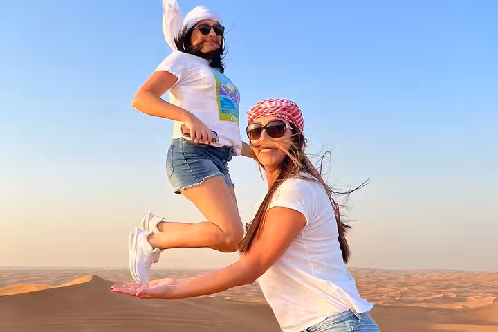 Two women joyfully posing on Abu Dhabi golden sand dunes during an exciting desert safari adventure tour