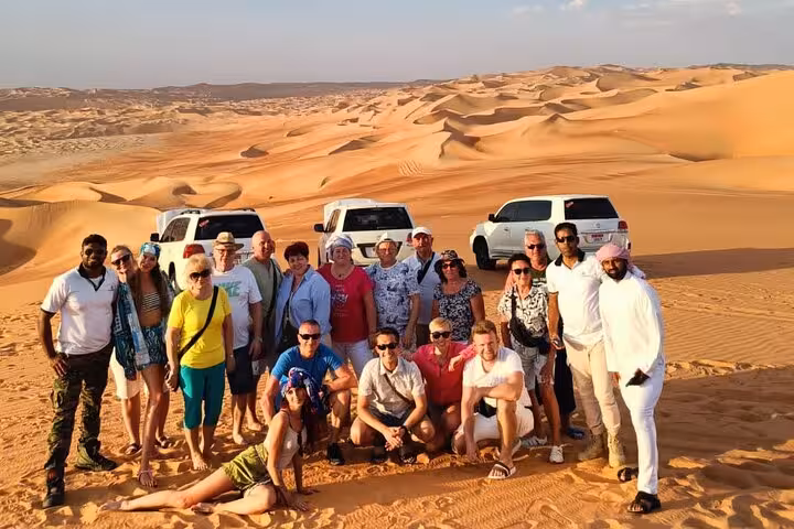 A group of tourists posing together on golden sand dunes during an Abu Dhabi desert safari with 4x4 vehicles
