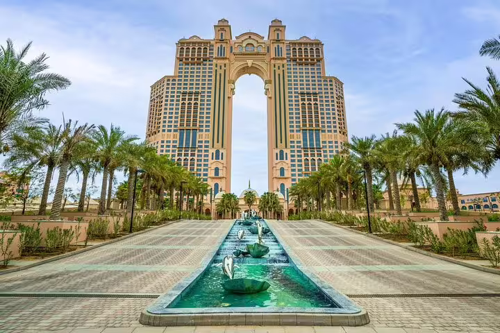 Grand architectural view of Abu Dhabi's iconic Etihad Towers framed by palm-lined walkways on a sunny day.