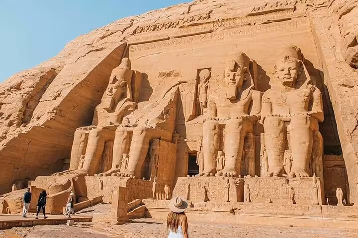Visitors at Abu Simbel Great Temple entrance with Ramses II statues, on a guided day trip from Aswan