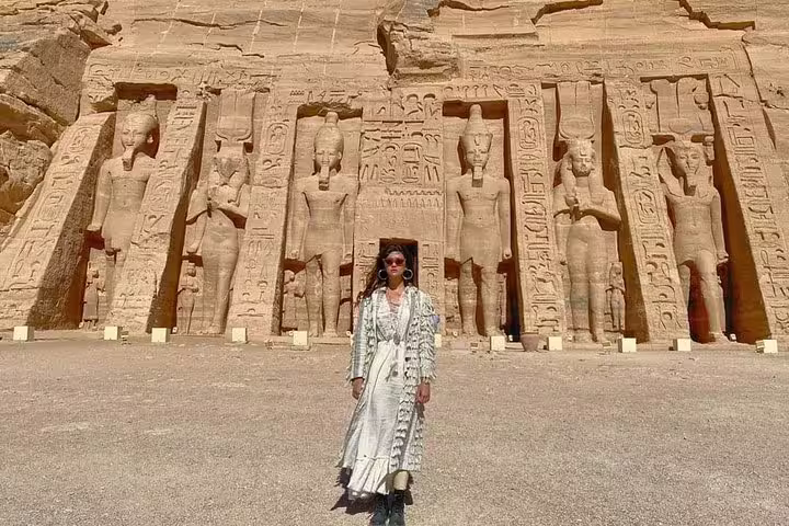 Visitor posing before Abu Simbel Temple statues on a day tour from Aswan, ancient Egyptian reliefs and columns