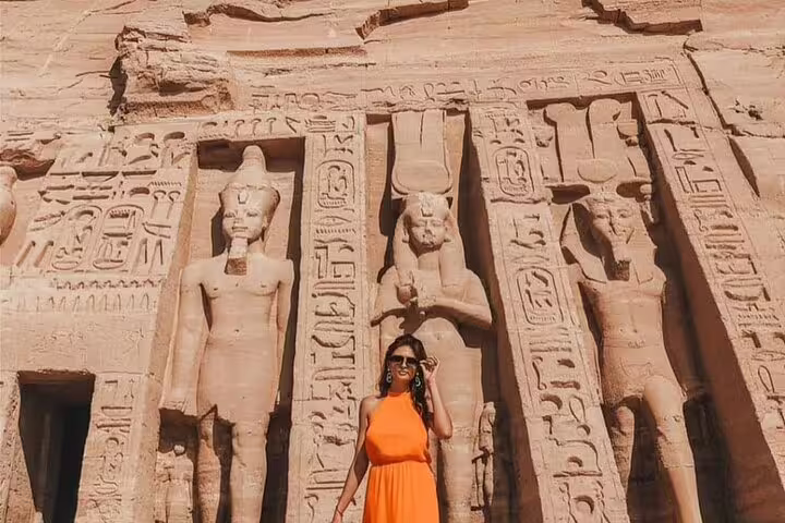 Visitor in orange dress by Abu Simbel temple carvings, highlight on full-day guided tour from Aswan