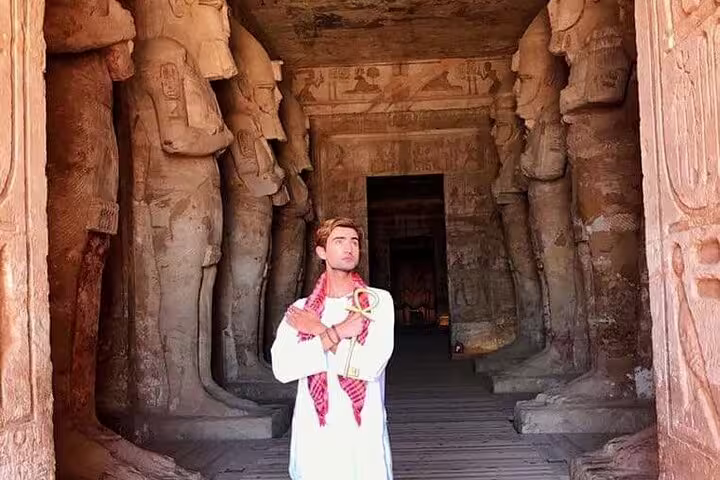 Traveler inside Abu Simbel temple hypostyle hall on day tour from Aswan, carved statues and hieroglyphs