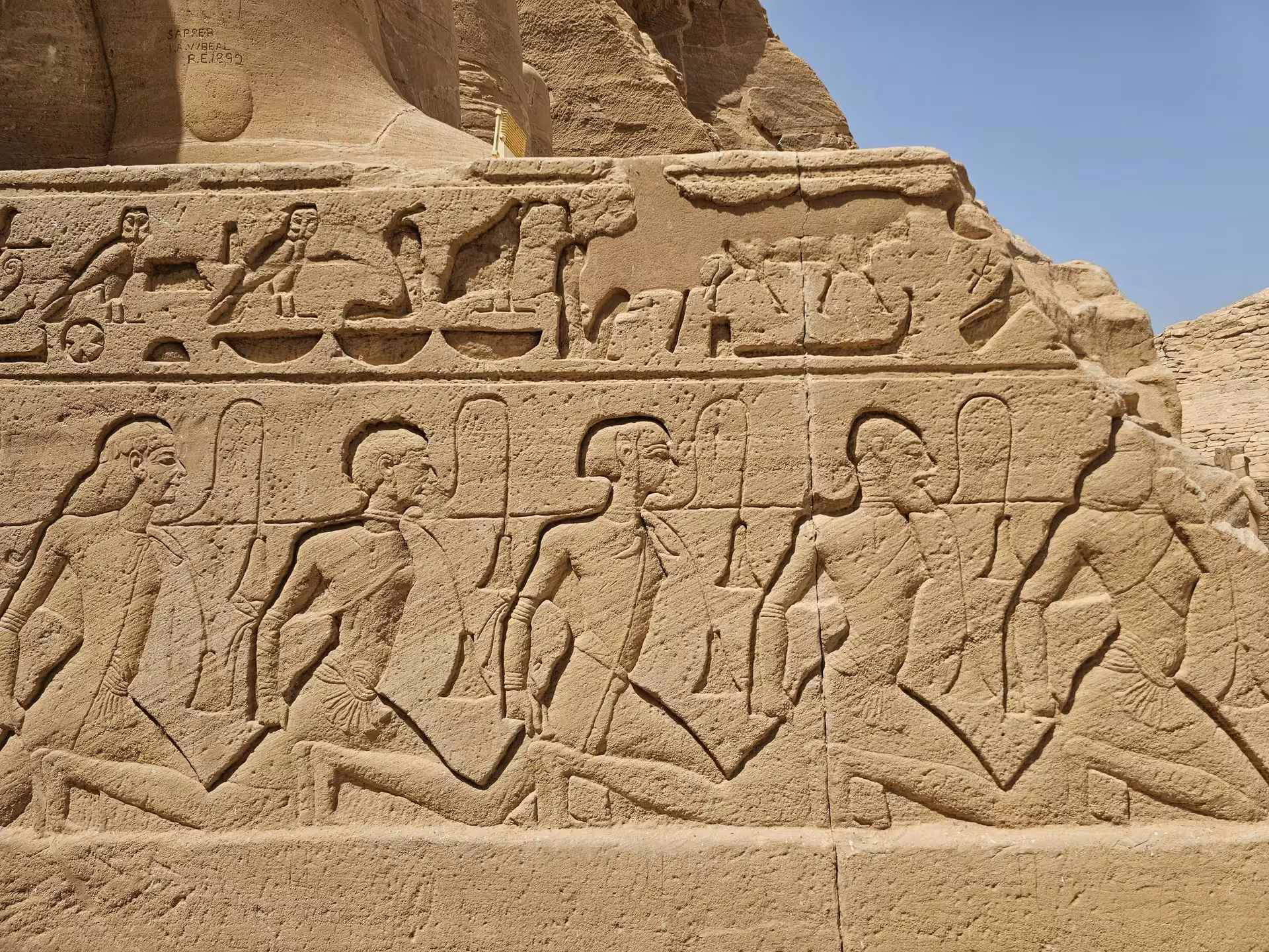 Ancient Egyptian relief carvings of prisoners and hieroglyphs on Abu Simbel temple stone wall