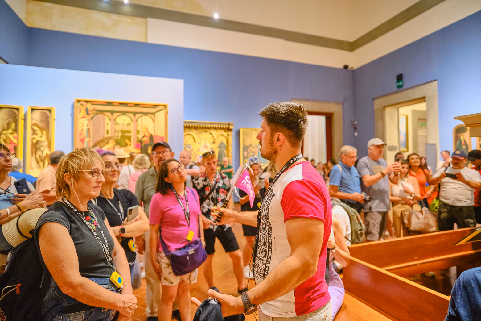 Tour guide leading a group in Accademia Gallery, Florence, with vibrant art pieces in the background.