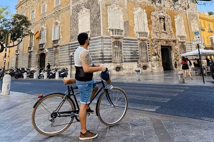Adult rider with classic city bike pauses by historic baroque building, perfect city bike rental for touring