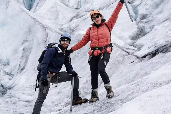 Two excited adventurers in helmets and crampons celebrating on Iceland glacier lagoon ice hiking tour