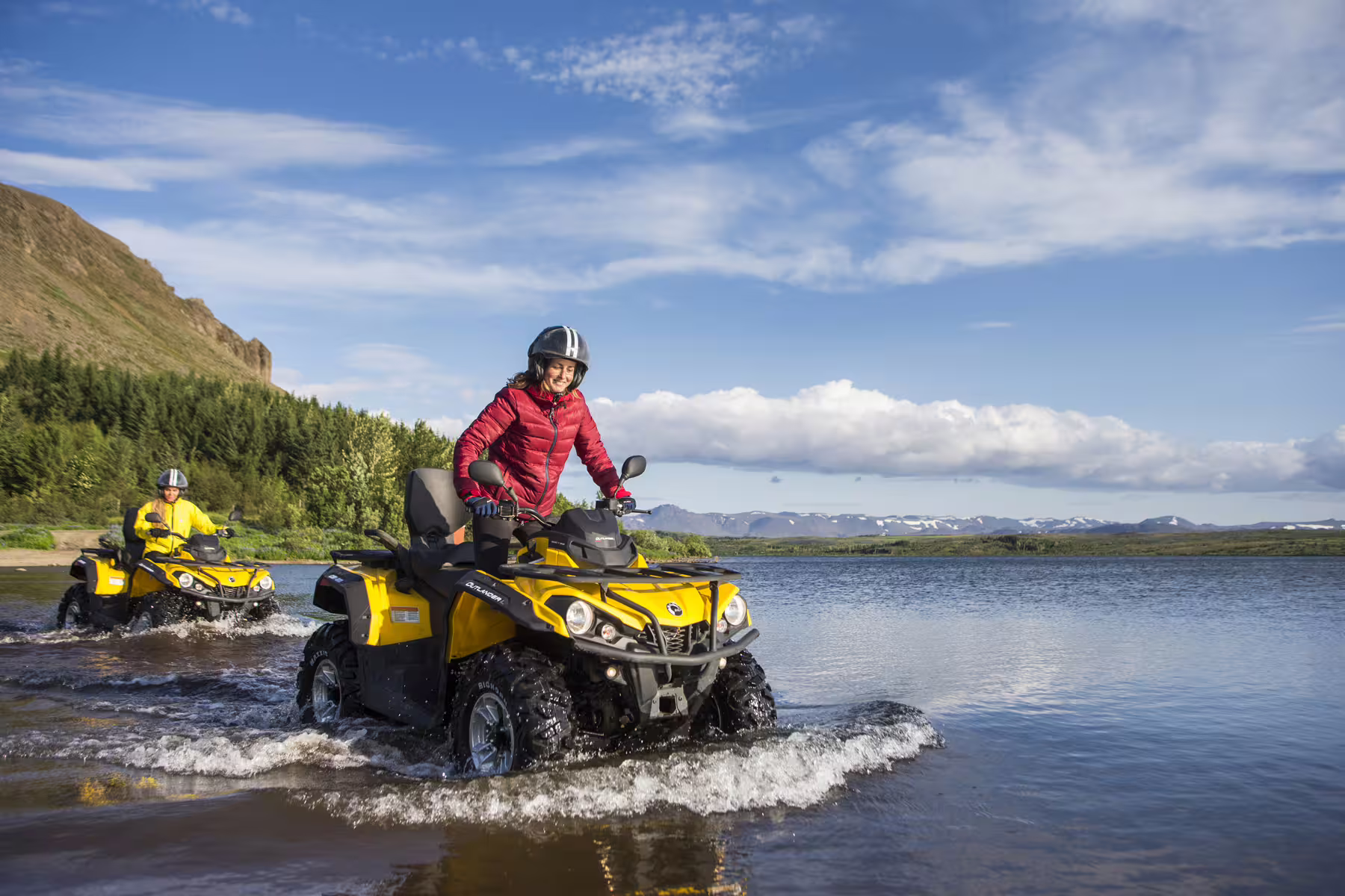 Two adventurers ride yellow ATVs through a scenic river landscape, perfect for an exhilarating ATV and caving tour.