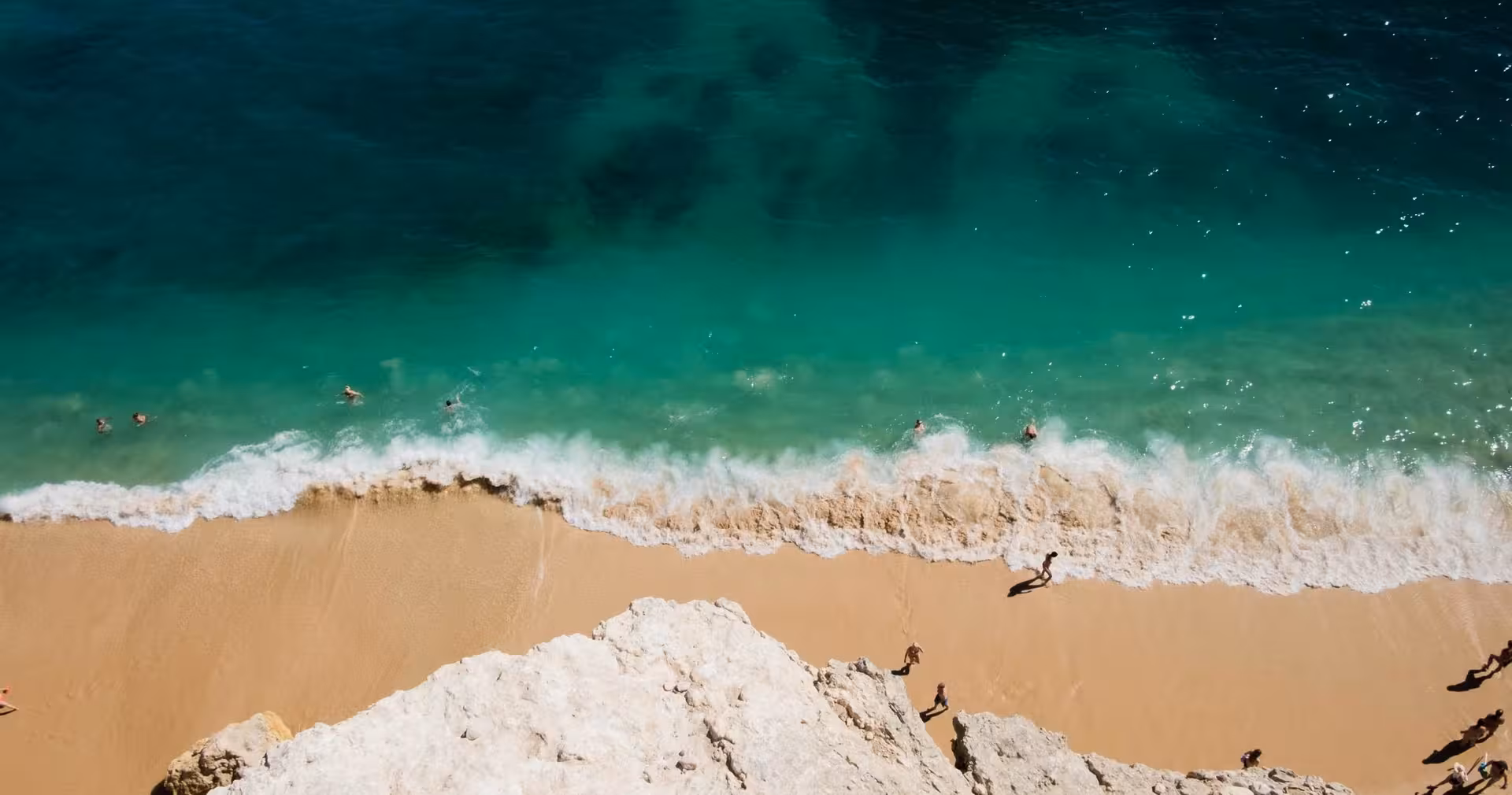 Aerial view of a serene beach with golden sand, turquoise waves, and people enjoying the sun and surf.