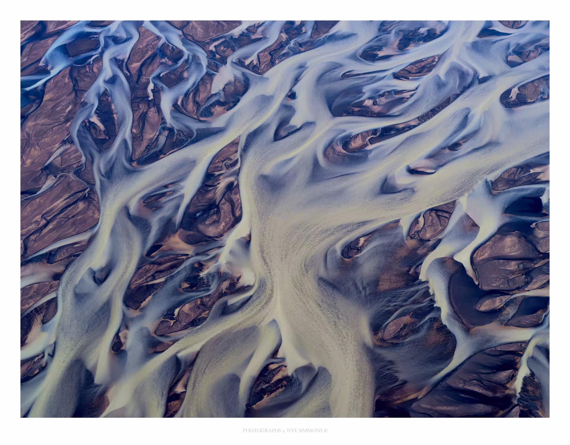 Aerial view of braided glacial river channels with blue silty water weaving through dark sediment in South Iceland