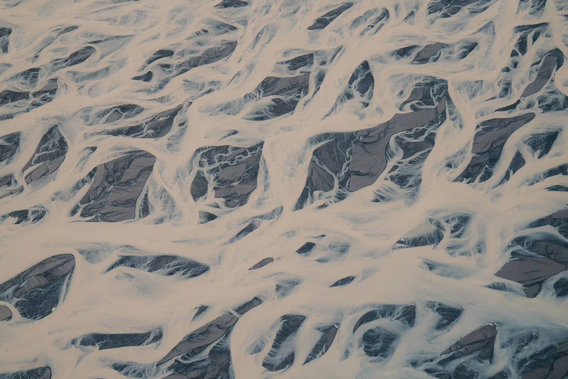 Aerial view of braided glacial river channels with white silty water weaving through dark sediment in South Iceland