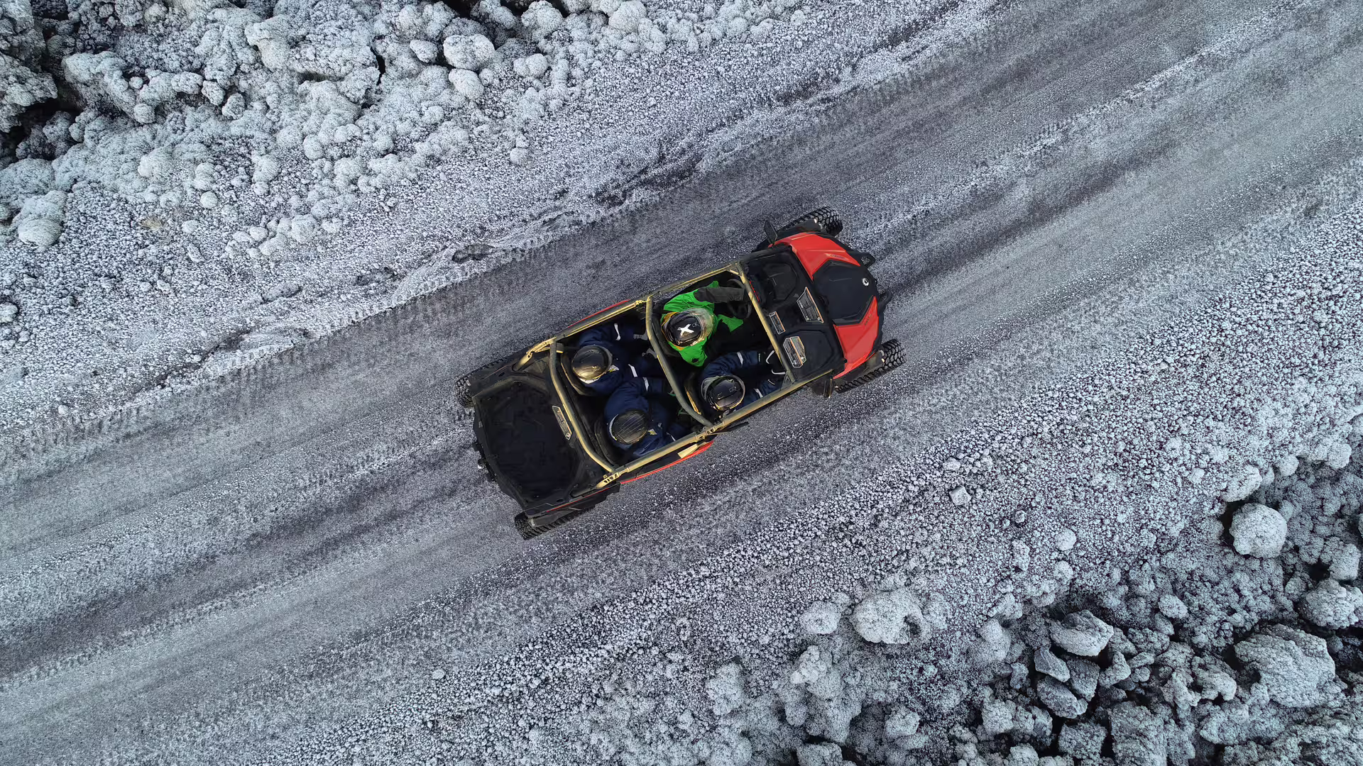 Aerial view of red off-road buggy with passengers driving on volcanic lava beach terrain