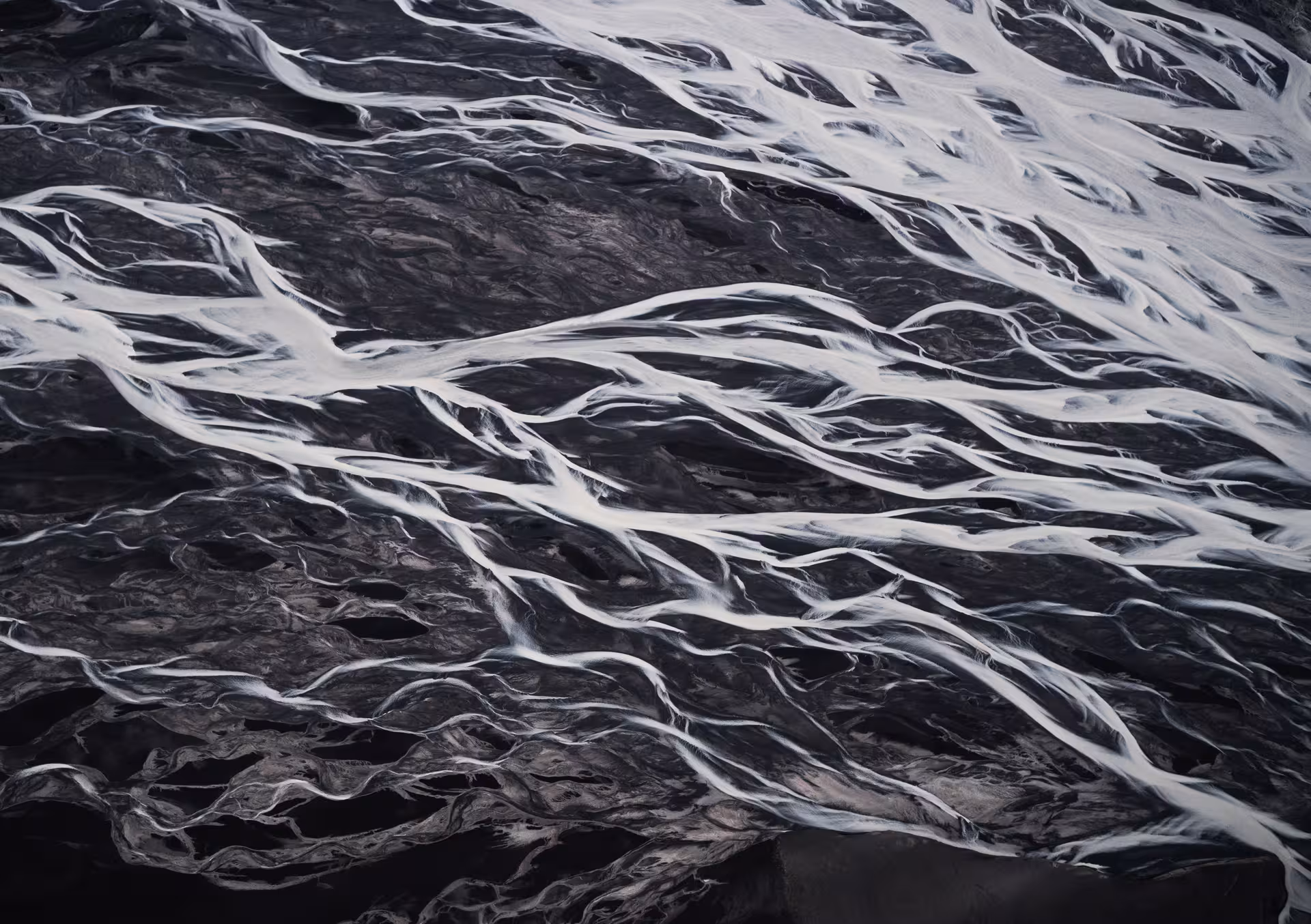 Aerial view of braided glacial rivers flowing over dark volcanic black sand in Iceland
