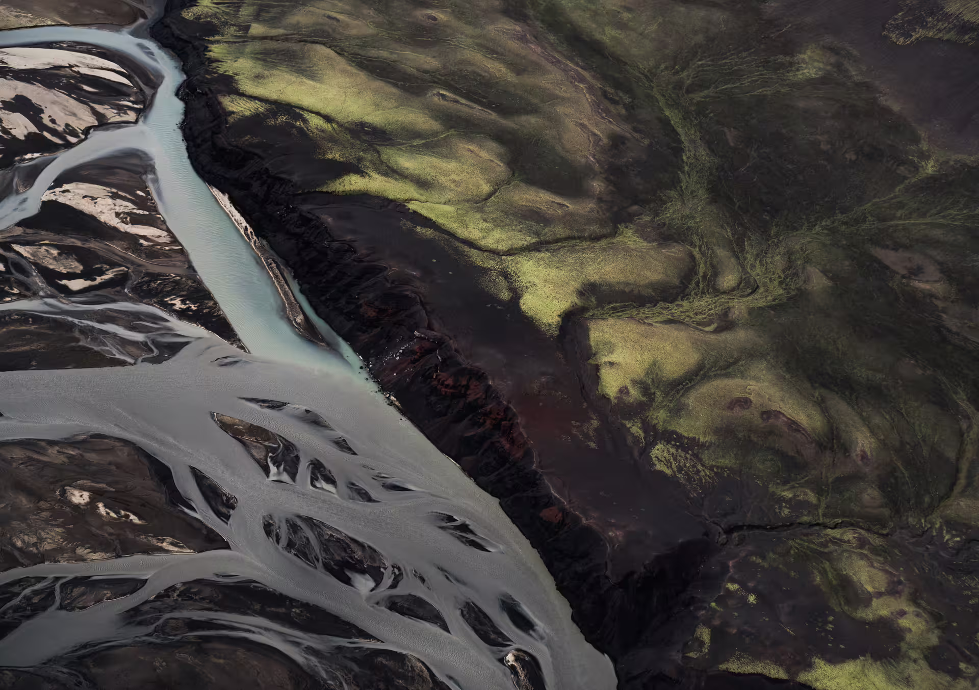 Aerial view of braided glacial rivers and green moss-covered lava fields in South Iceland