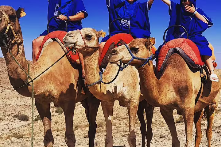 Camel ride in Agafay Desert with riders in blue robes, part of quad bike and dinner show excursion
