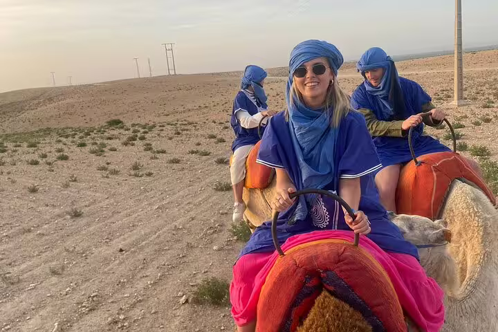 Group camel trekking in Agafay Desert at sunset from Marrakech, riders in blue outfits enjoying the dunes