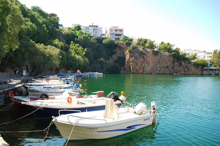Idyllic boats moored in the serene waters of Agios Nikolaos, framed by lush foliage and rocky cliffs on a sunny day.