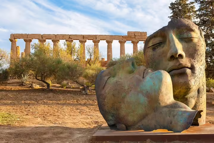 Modern bronze face sculptures set before ancient temple columns in Agrigento’s Valley of the Temples, Sicily