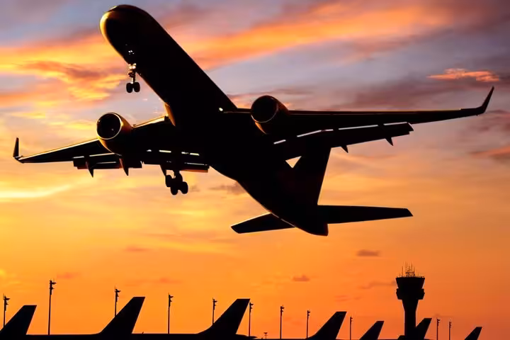 Commercial airplane taking off at sunset over Keflavik Airport with air traffic control tower silhouette