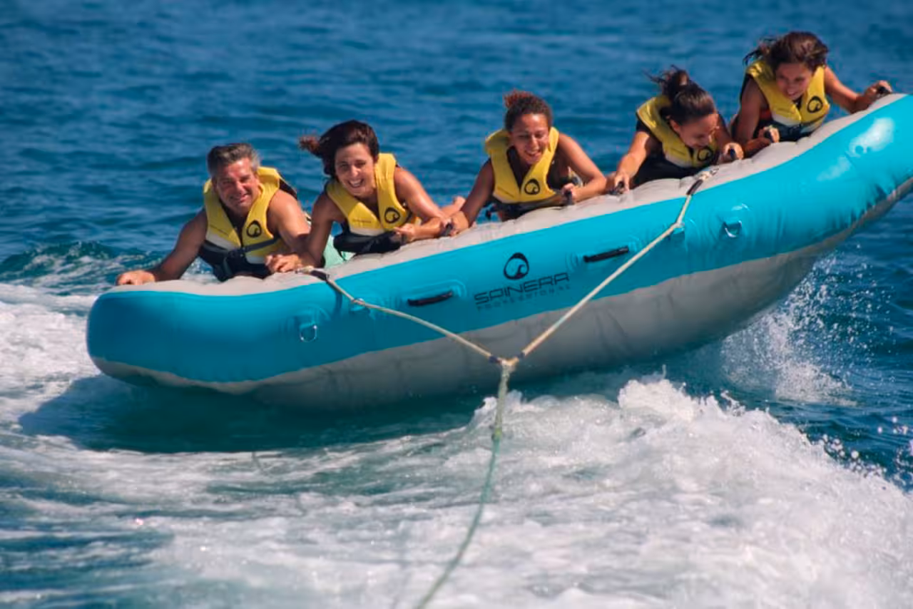 Family enjoying thrilling Airstream banana boat ride, bouncing over blue sea with spray and bright yellow life jackets