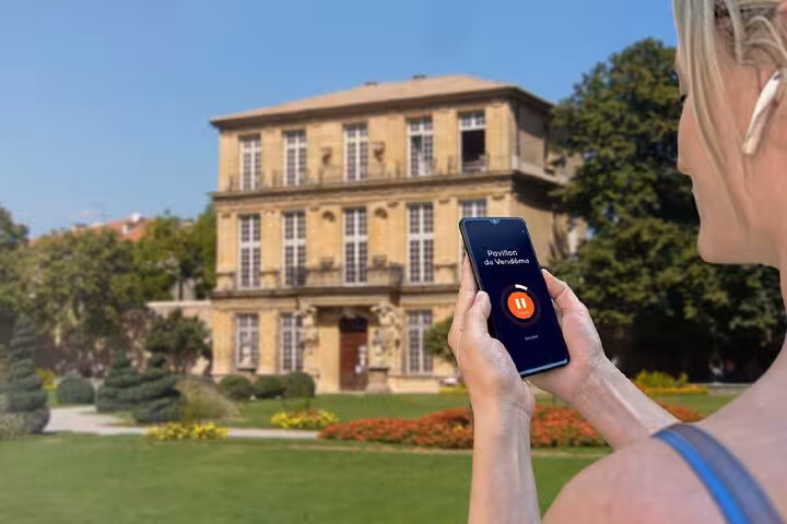 Woman holding smartphone with audio guide app in front of Pavillon de Vendôme in Aix-en-Provence