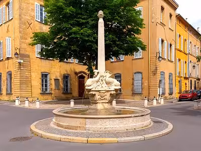 Historic fountain with swan sculptures in a sunny square surrounded by yellow buildings in Aix-en-Provence