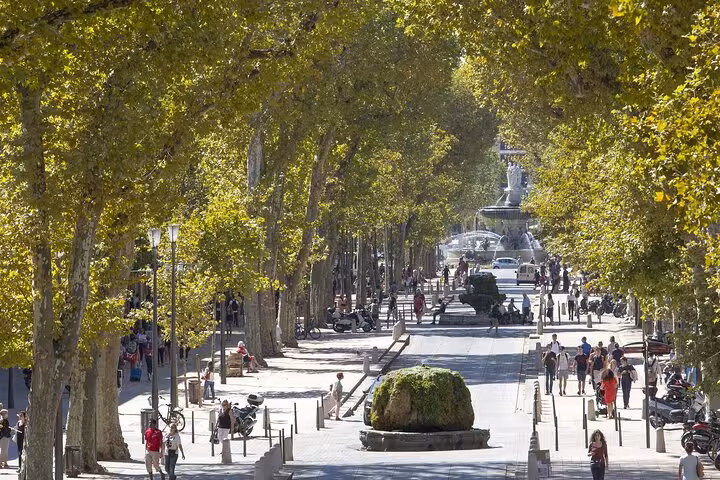 Tree-lined boulevard in Aix-en-Provence with fountain and pedestrians on sunny day