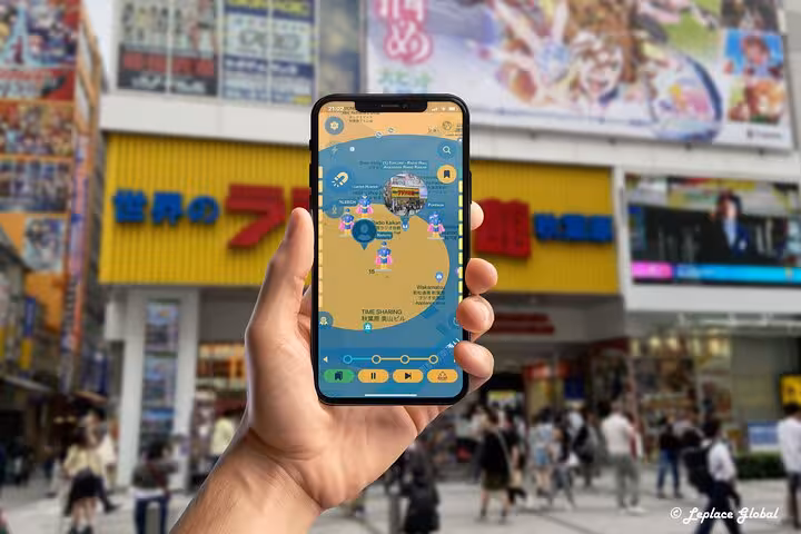 Hand holding smartphone with Akihabara walking tour mobile app map in front of iconic Tokyo gaming district street