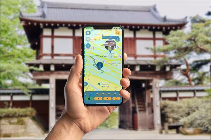 Hand holding smartphone with GPS walking tour app in front of traditional Japanese temple gate in Akita City