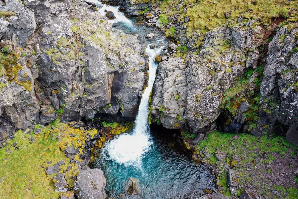 Aerial view of a stunning Iceland waterfall cascading through mossy volcanic rocks on Akrafjall Troll Mountain guided trek.