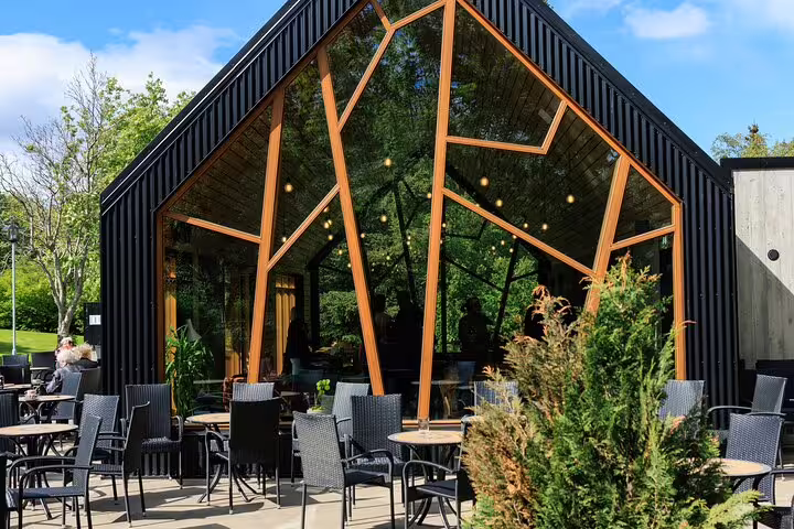 Modern glass and wood botanical garden café with outdoor seating surrounded by lush greenery in Akureyri