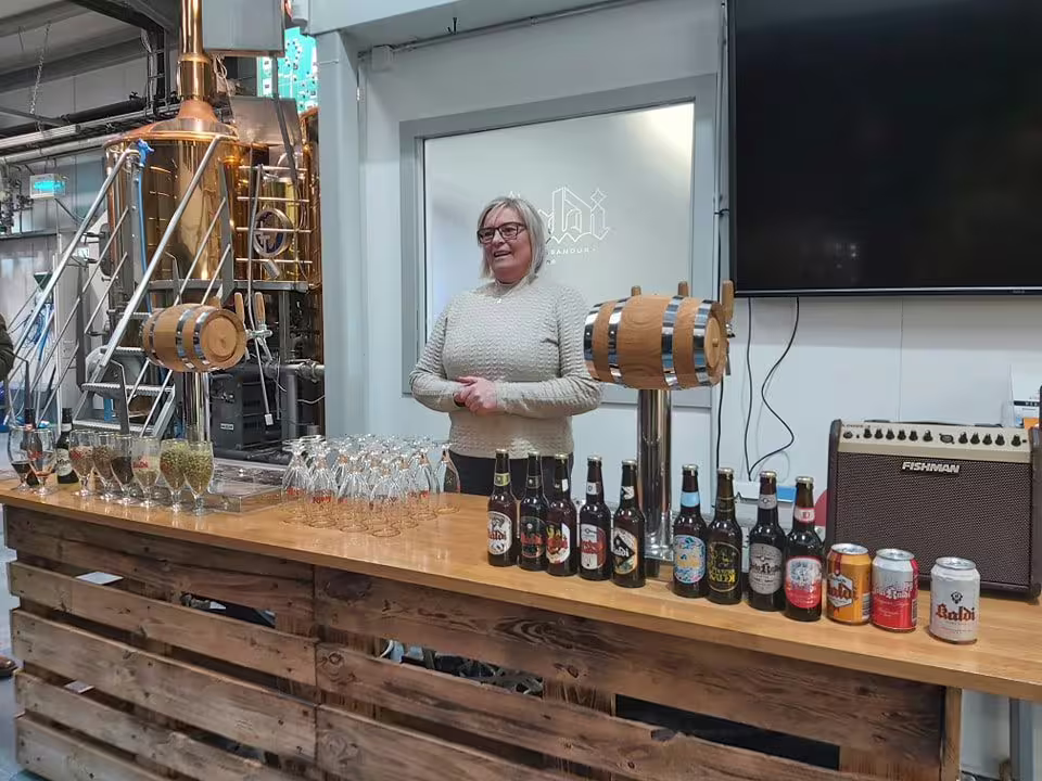Woman standing behind brewery bar with Baldi craft beer bottles, glasses, and wooden barrel tap in Akureyri
