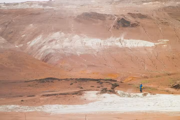 Lone hiker in blue jacket exploring red geothermal landscape near Akureyri, Iceland