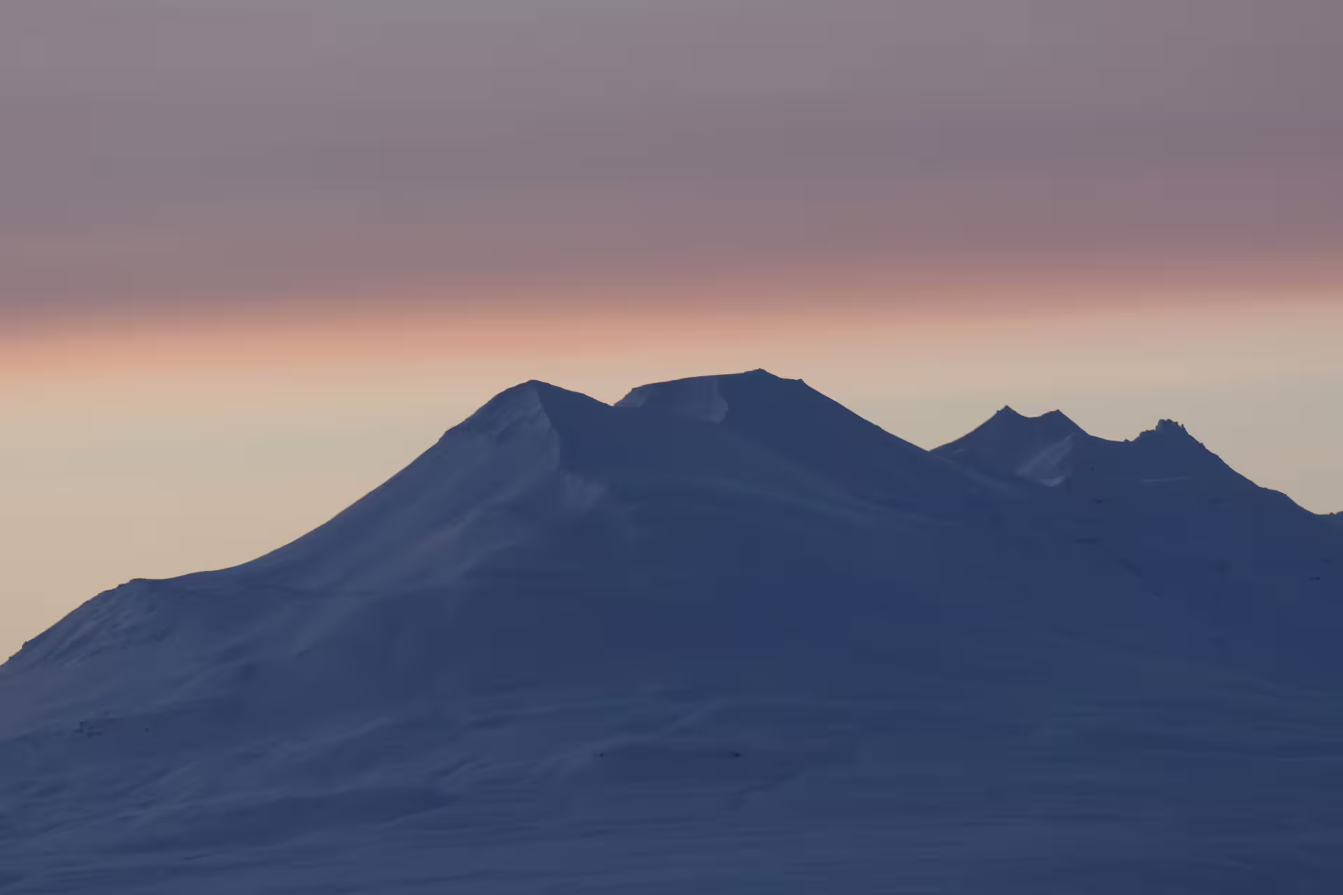 Snow-covered mountain peaks silhouetted against a pink and orange sunset sky near Akureyri, Iceland