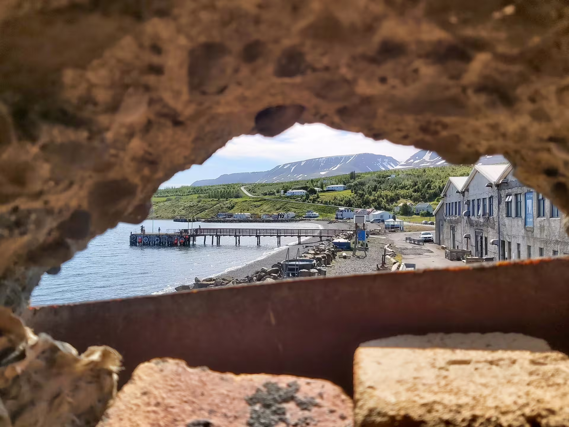 View through rocky hole of Akureyri fjord pier, coastal buildings, and snow-capped mountains in Iceland