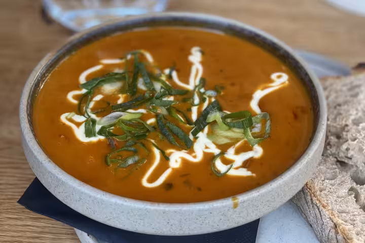 Bowl of creamy orange soup topped with sautéed leeks and cream drizzle, served with crusty bread