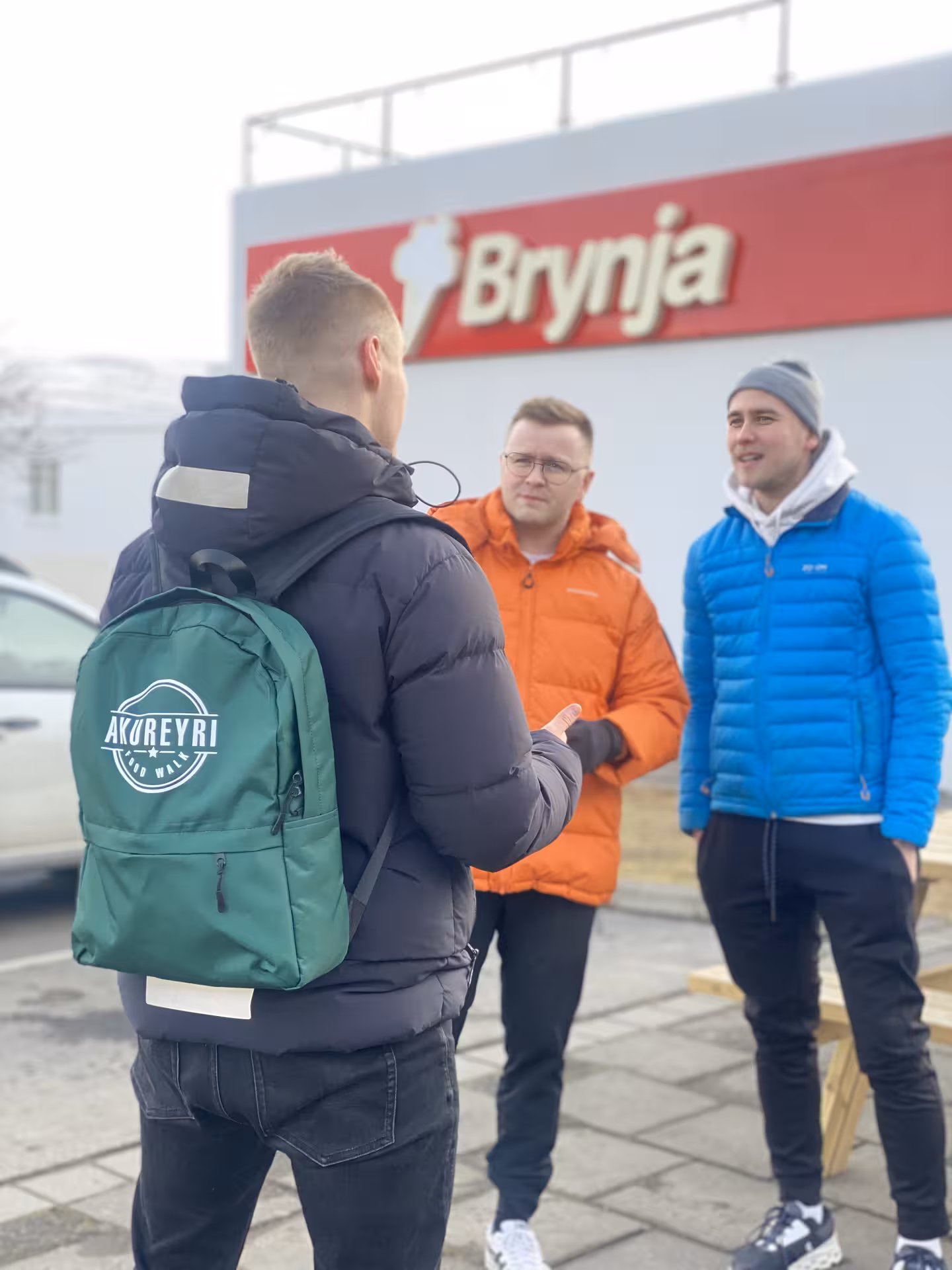 Tour guide with Akureyri Food Walk backpack talking to two men outside Brynja store in Iceland