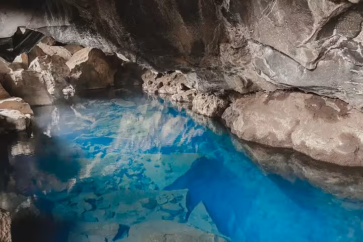 Crystal clear blue geothermal cave pool with steaming water surrounded by volcanic rock in Iceland