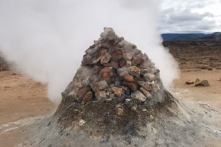 Steam rising from a volcanic fumarole mound with red and grey rocks at a geothermal area near Akureyri, Iceland