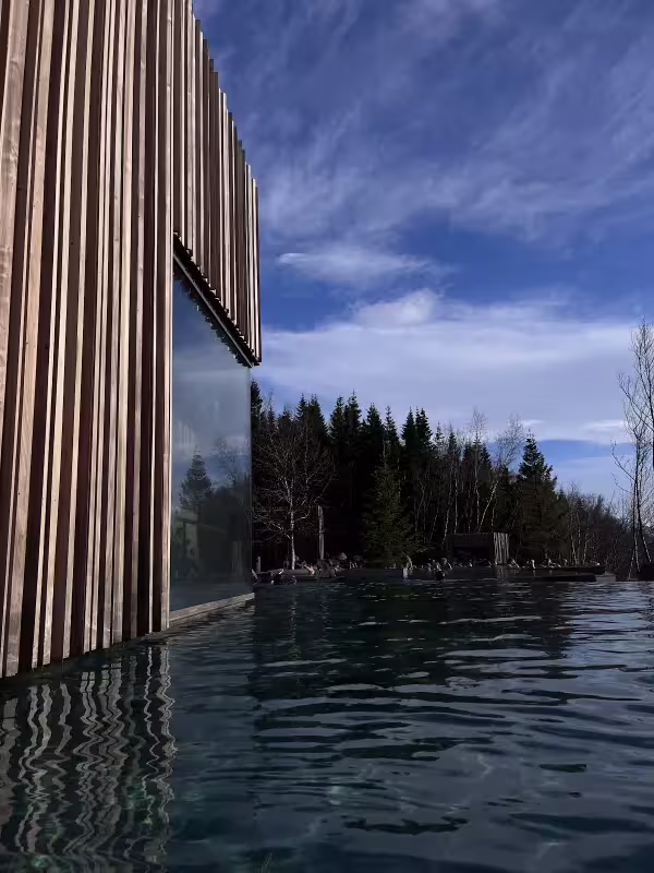 Infinity pool beside modern wooden clad building with evergreen forest and blue sky in Akureyri Iceland
