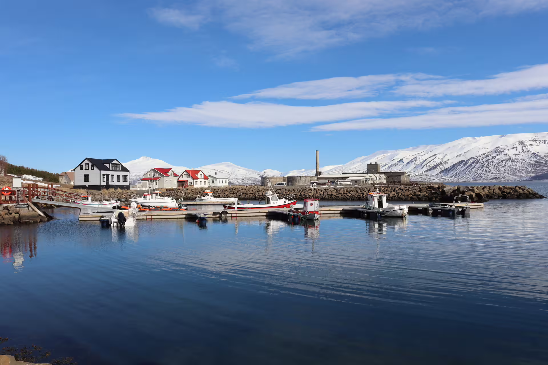 Small fishing boats docked at Akureyri harbor with colorful houses and snow-capped mountains in background