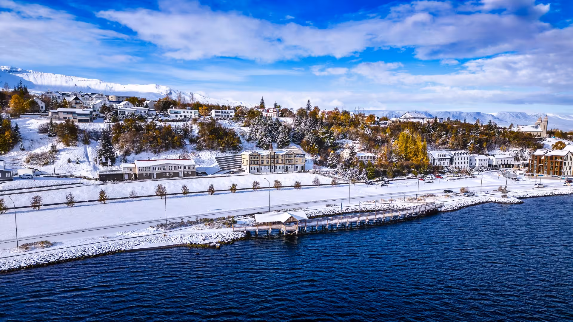 Aerial winter view of Akureyri harbor waterfront with snow-covered buildings and mountains in Iceland