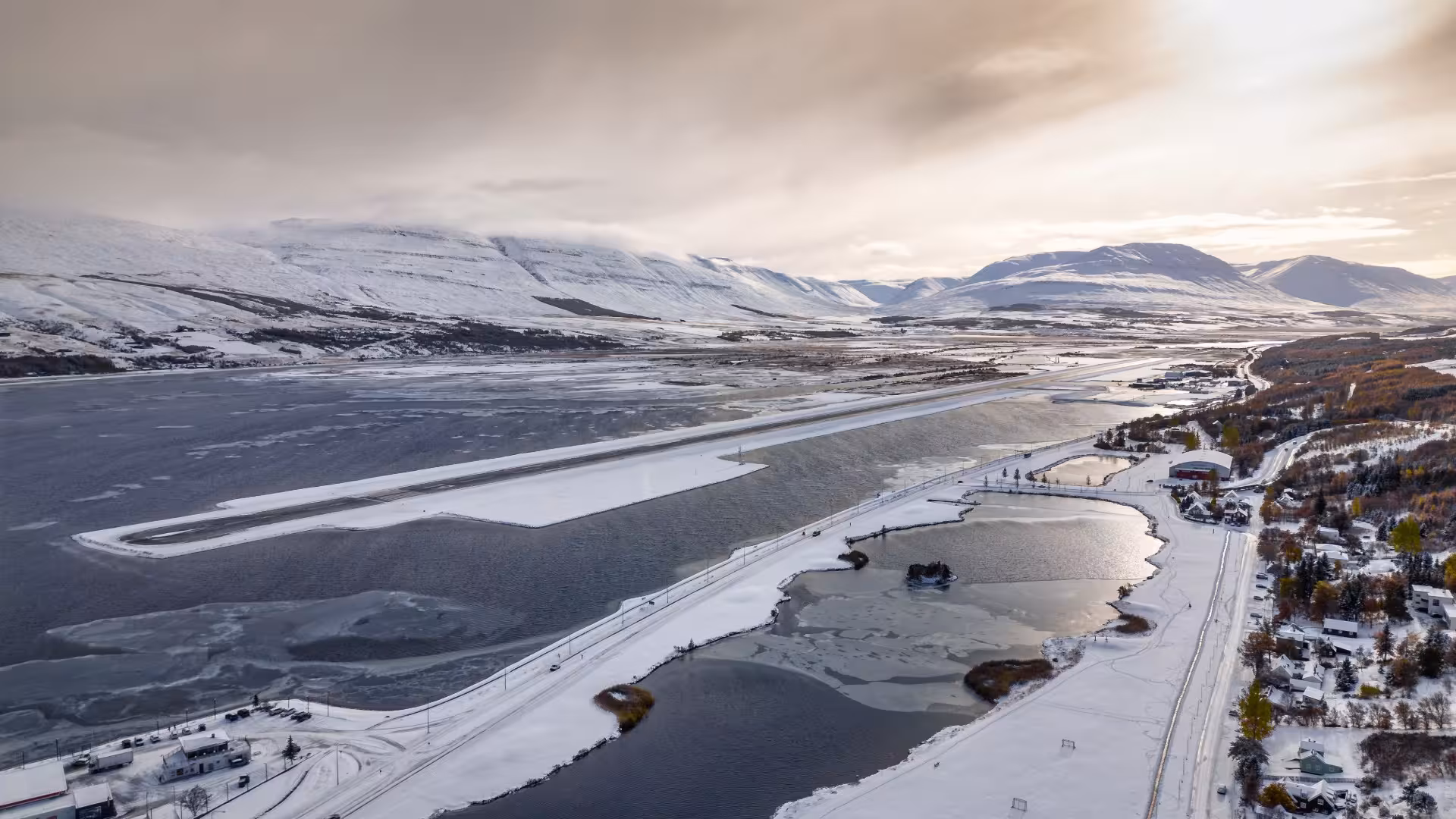 Aerial winter view of Akureyri airport runway beside fjord with snow-capped mountains in background
