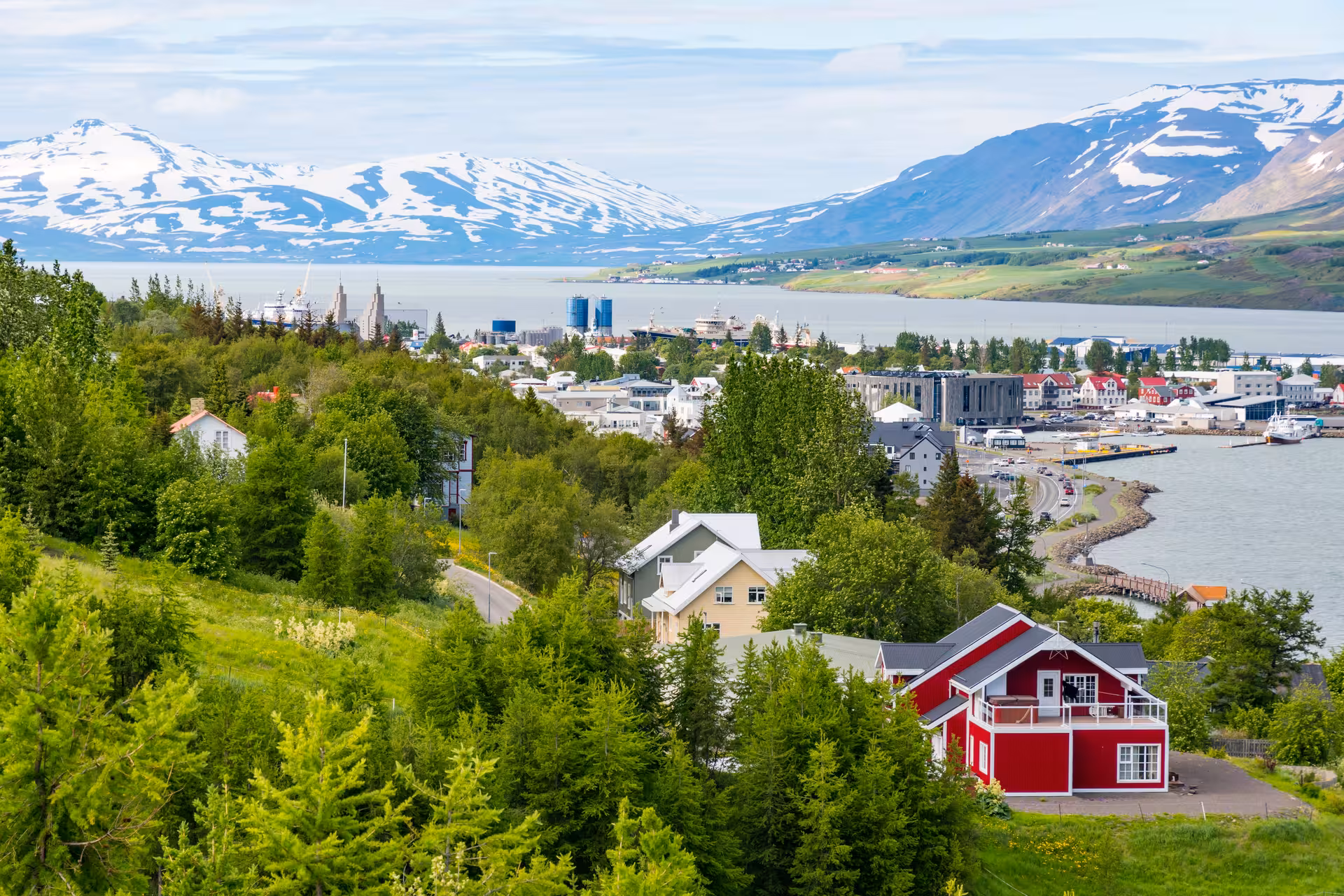 Scenic view of Akureyri with colorful houses, lush greenery, and snow-capped mountains in Iceland's charming town.