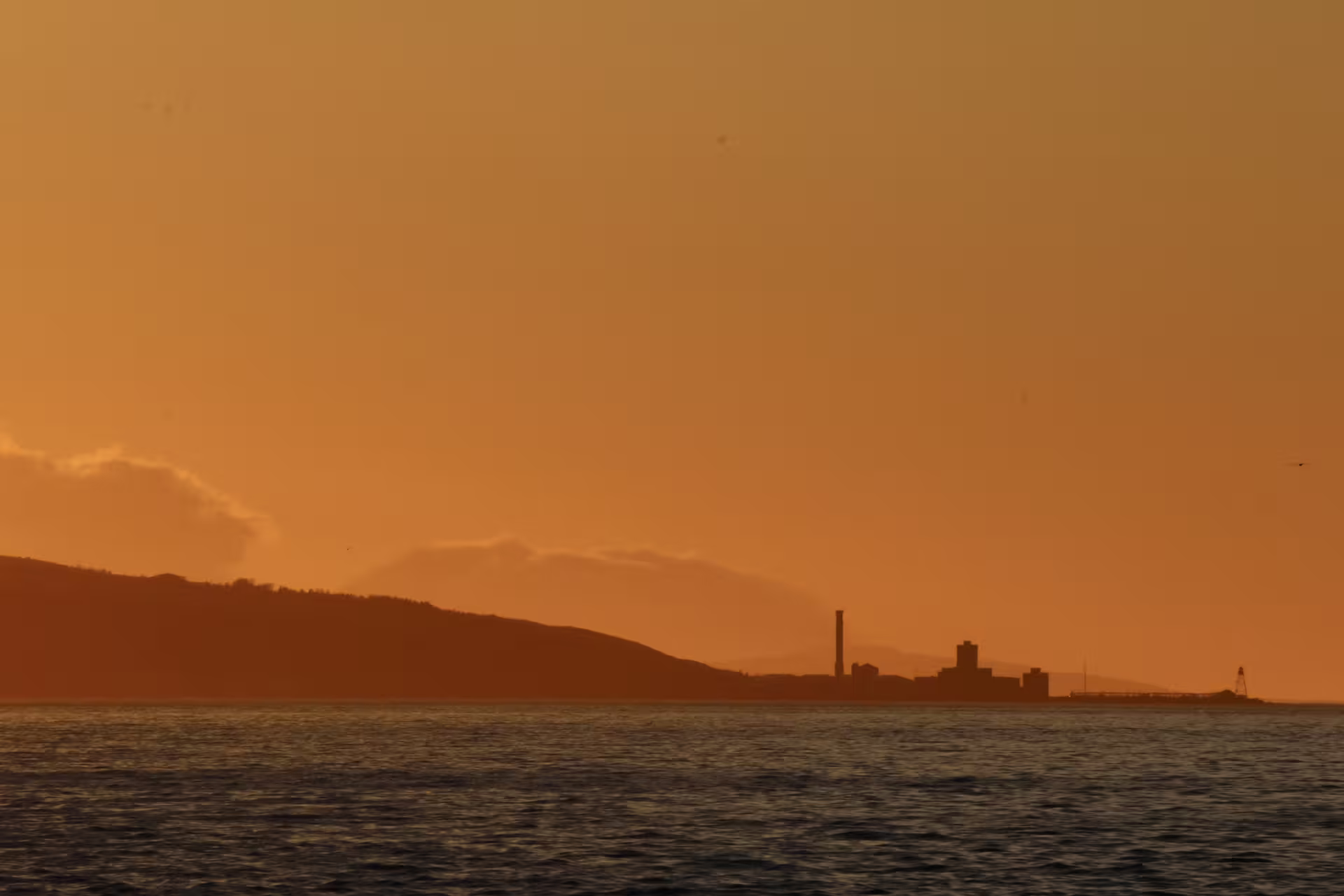 Industrial coastline silhouette under golden midnight sun sky viewed from whale watching boat in Akureyri