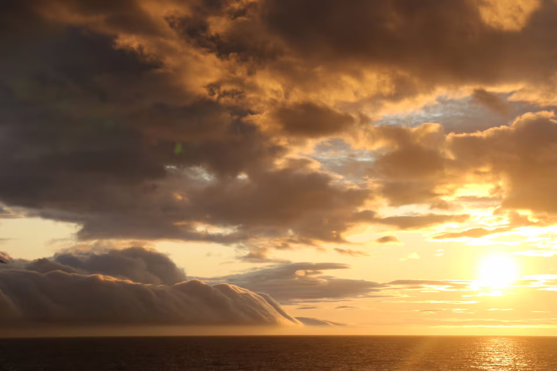 Golden midnight sun setting over calm ocean with dramatic storm clouds in Akureyri, Iceland