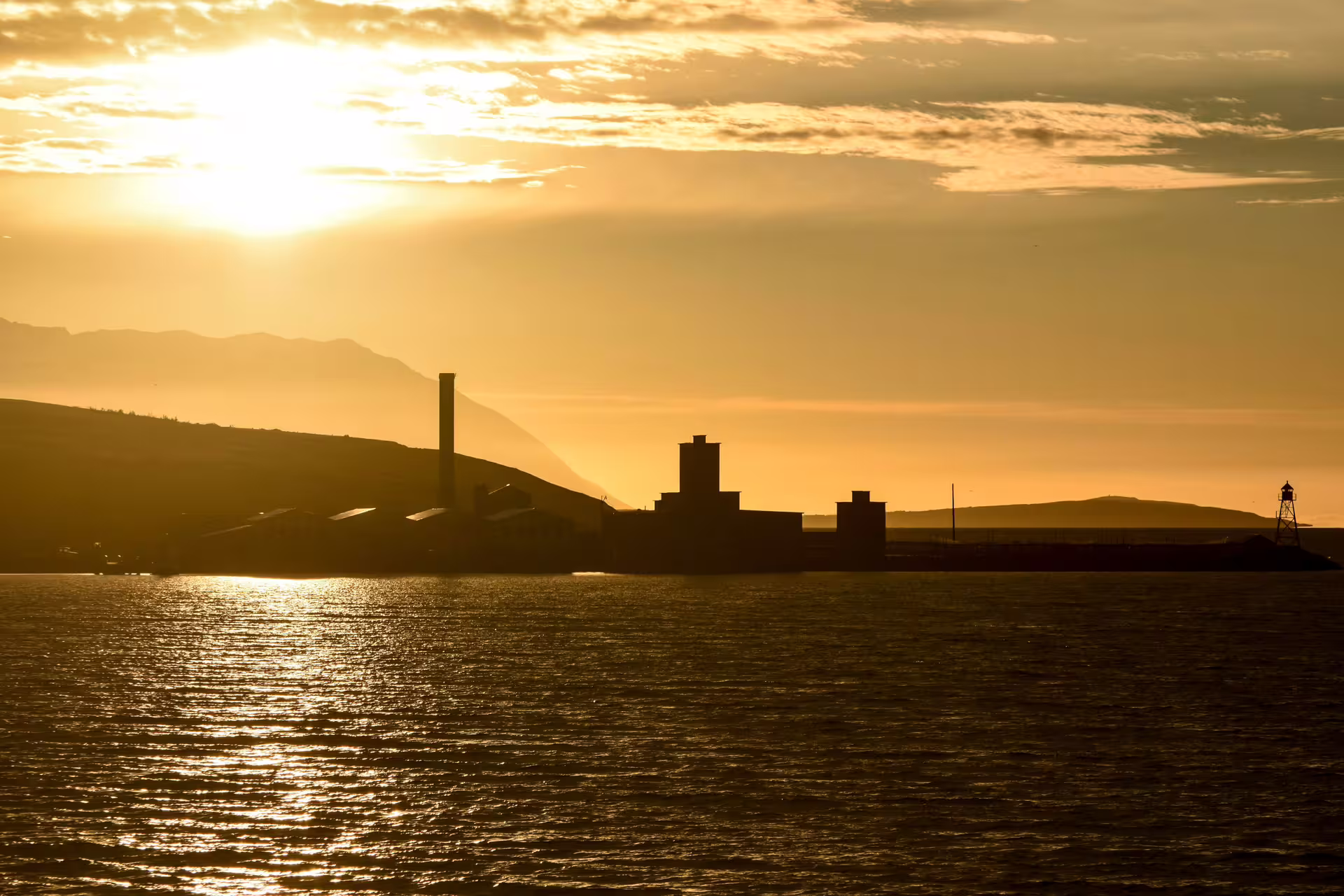 Industrial silhouette and lighthouse on Akureyri waterfront glowing under midnight sun golden sky