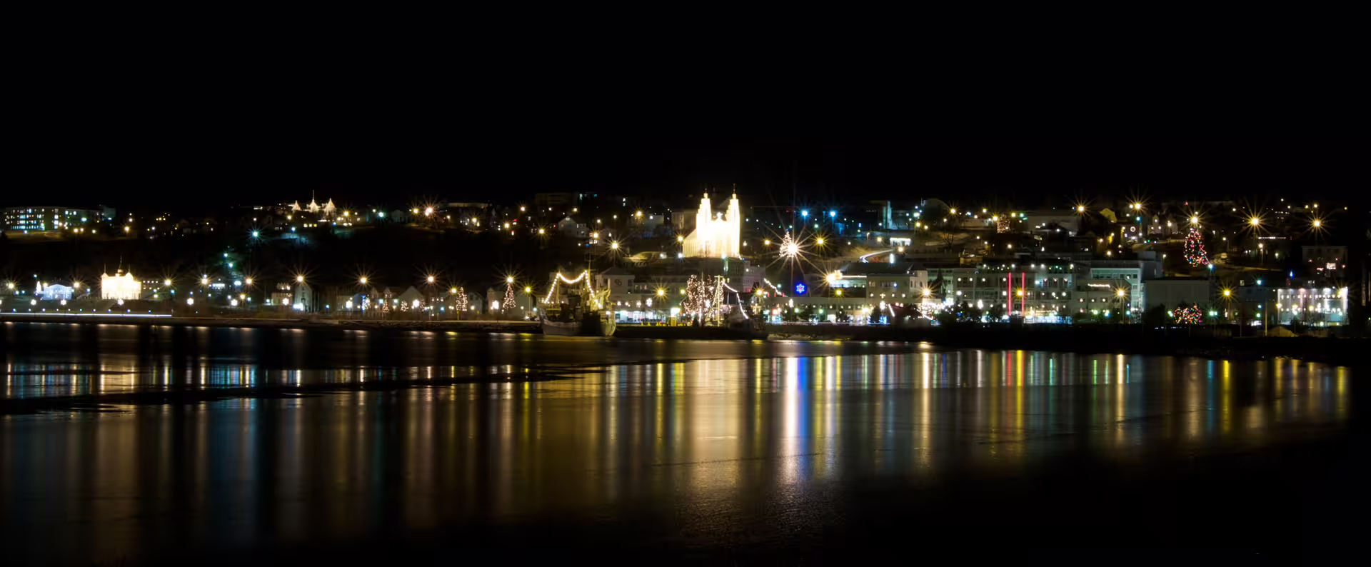 Akureyri city lights reflecting on calm water at night, illuminated cathedral and harbor visible