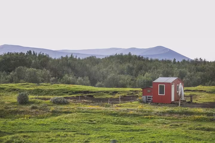Red cabin on green Icelandic countryside with mountains and trees near Akureyri